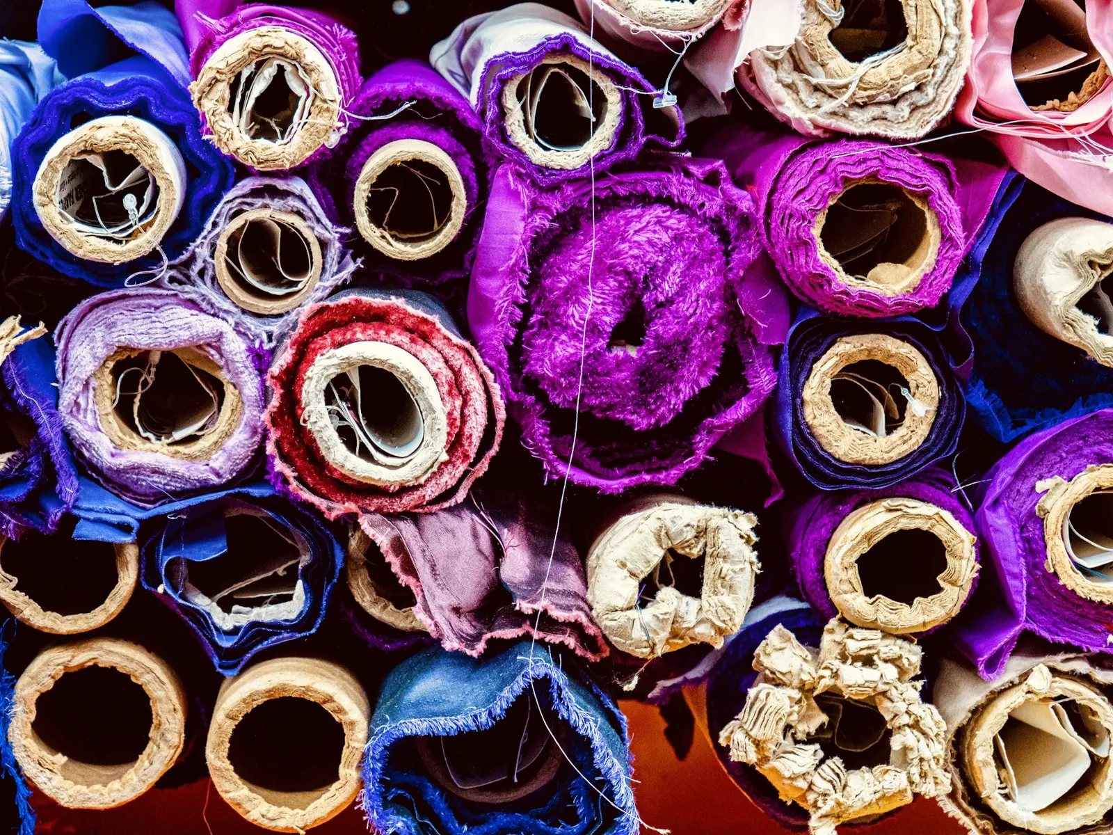Rollos de tela de colores apilados, vistos desde arriba, en un taller textil mayorista